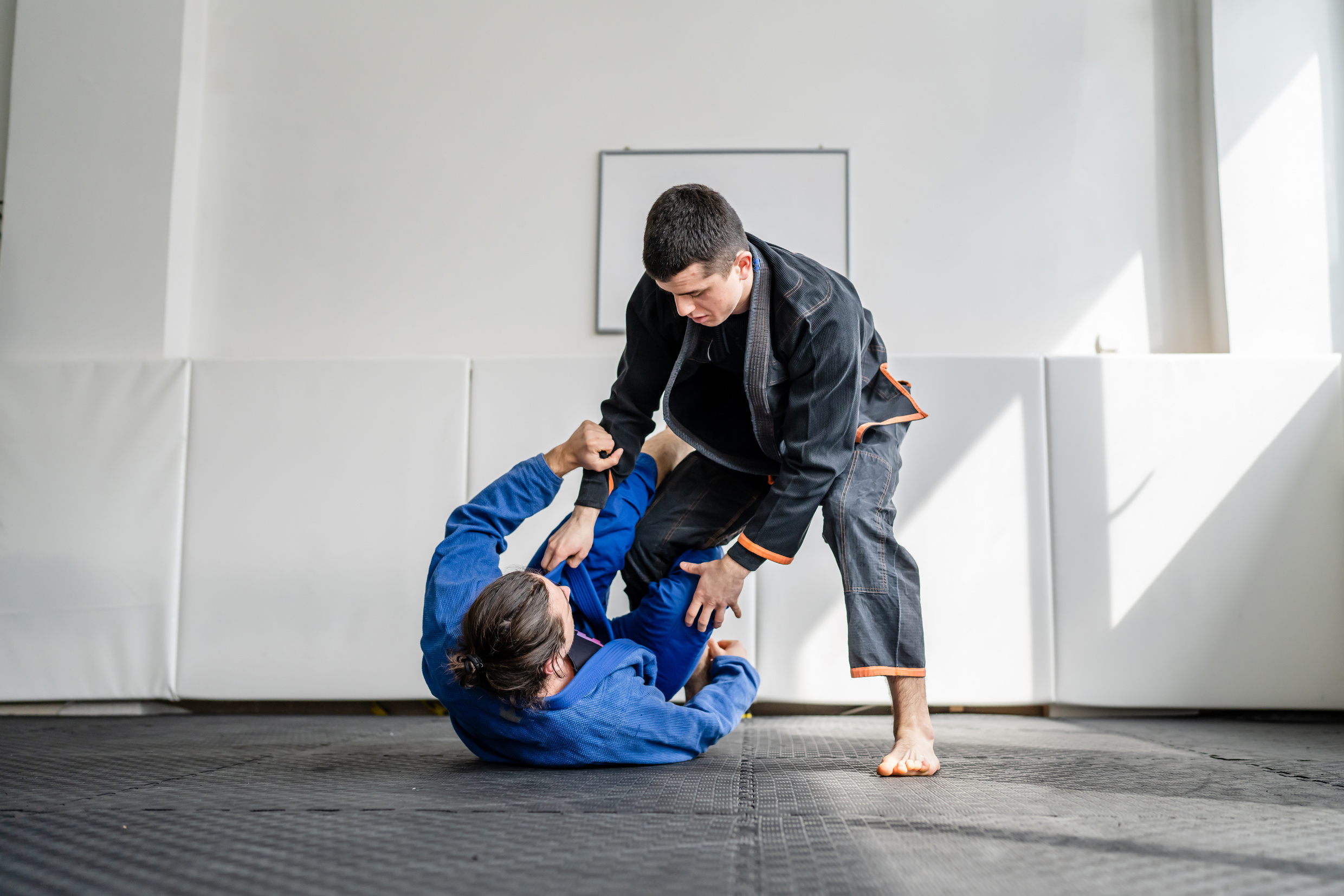Two brazilian jiu jitsu BJJ athletes training at the academy martial arts ground fighting sparring wear kimono gi sport uniform on the tatami mats sports jiujitsu and self-defense concept copy space